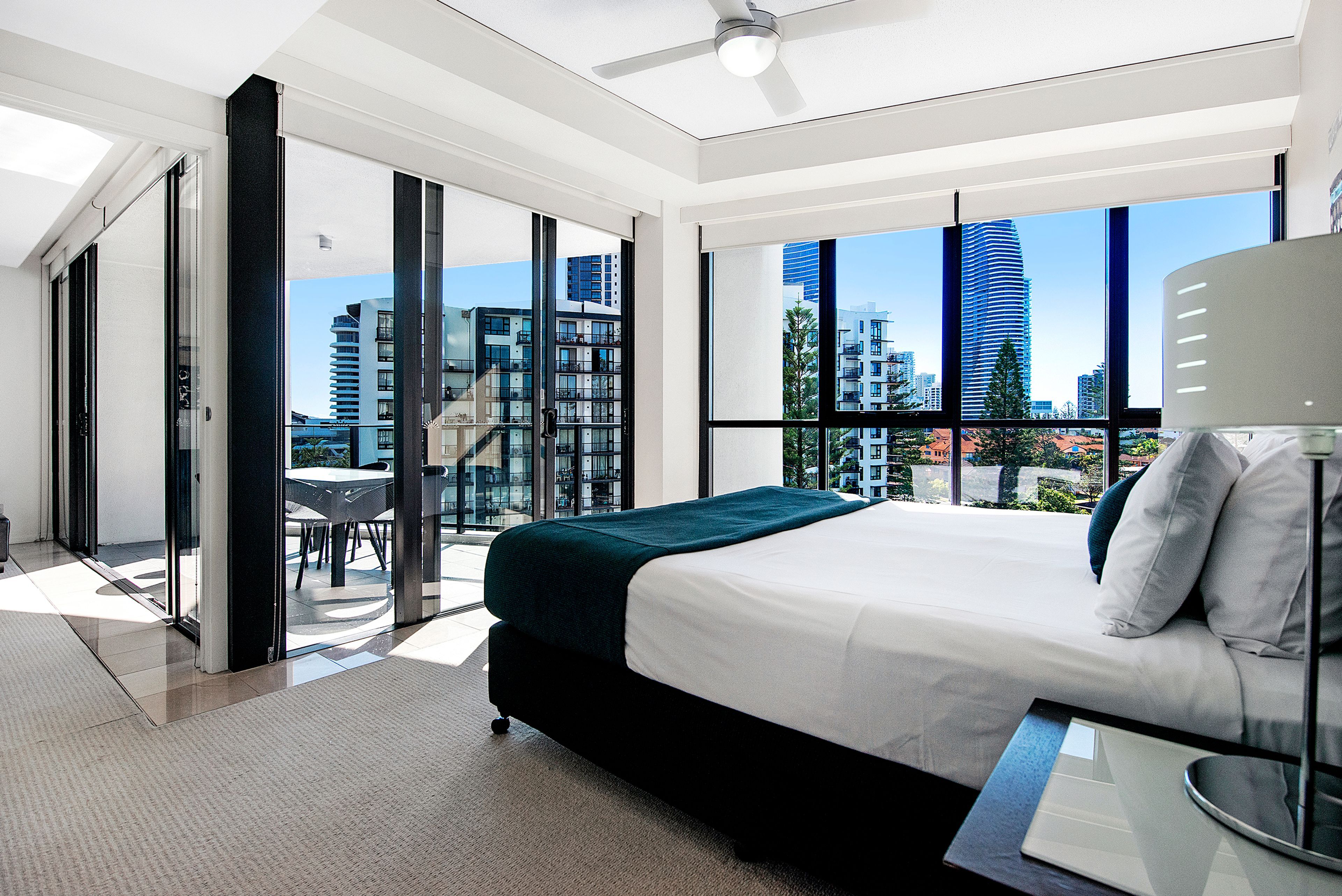 A modern hotel room with a large bed, a balcony with a view of the city, and a dining area with a table and chairs.