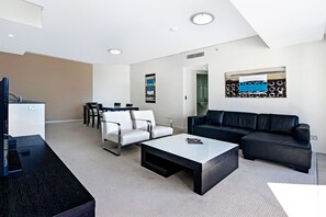 A modern living room with a black sofa, white chairs, a coffee table, and a dining area with a table and chairs.