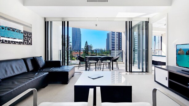 A modern living room with a black leather sofa, a glass coffee table, and a TV on a stand. - Stunning 2 Bed Apartment in Sierra Grand - CoastHM (Broadbeach)