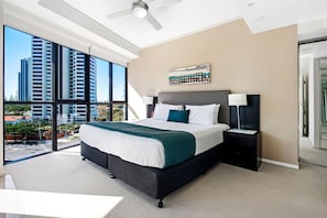 A modern hotel room with a large bed, a ceiling fan, a view of the city, and a large window. - Stunning 2 Bed Apartment in Sierra Grand (Broadbeach)