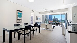 A modern hotel room with a dining area, a balcony with a city view, and a kitchenette. - Stunning 2 Bed Apartment in Sierra Grand - CoastHM (Broadbeach)