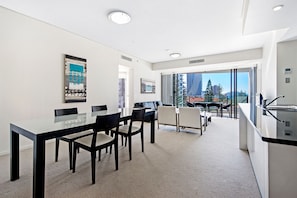 A modern hotel room with a dining area, a kitchenette, and a balcony with a city view. - Stunning 2 Bed Apartment in Sierra Grand (Broadbeach)