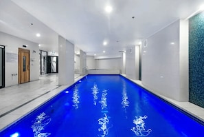 A swimming pool with a blue floor, surrounded by white walls and a tiled floor. - Stunning 2 Bed Apartment in Sierra Grand (Broadbeach)