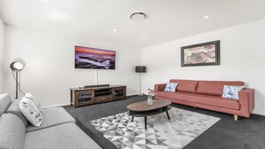 A modern living room with a grey sofa, a red sofa, a coffee table, and a TV on a wooden cabinet. - VISTA ELMS - THE VINTAGE HOLIDAY HOUSES (POKOLBIN)