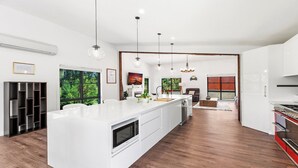 A modern kitchen with a large island, wooden flooring, and pendant lighting. - VISTA ELMS - THE VINTAGE HOLIDAY HOUSES (POKOLBIN)