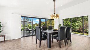 A modern dining area with a dark wooden table and black chairs, large windows offering a view of greenery and a building outside. - VISTA ELMS - THE VINTAGE HOLIDAY HOUSES (POKOLBIN)