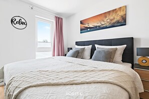Quarto moderno com uma cama grande, um letreiro que diz 'Relax', uma pintura e uma vista pela janela.