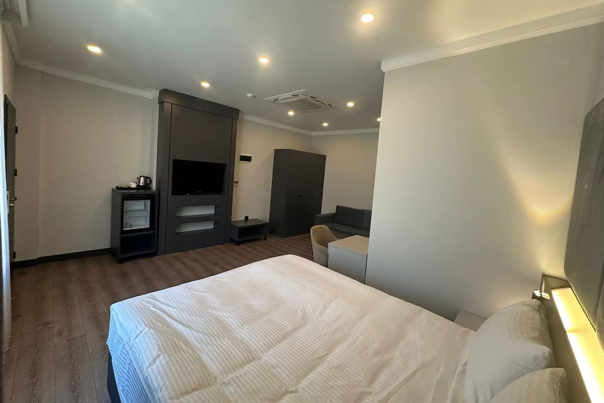 A hotel room with a bed, a TV, a wardrobe, and a seating area.