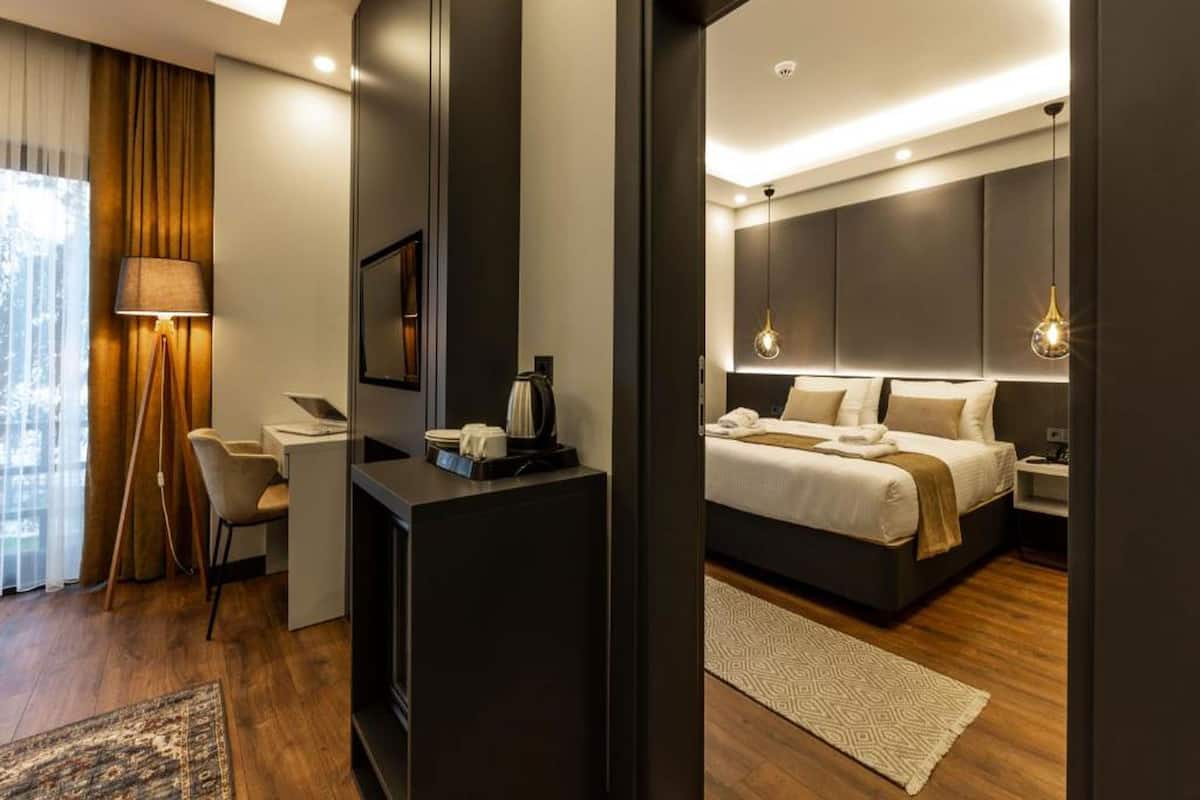 A modern hotel room with a bed, bedside table, lamp, and a view of the city.