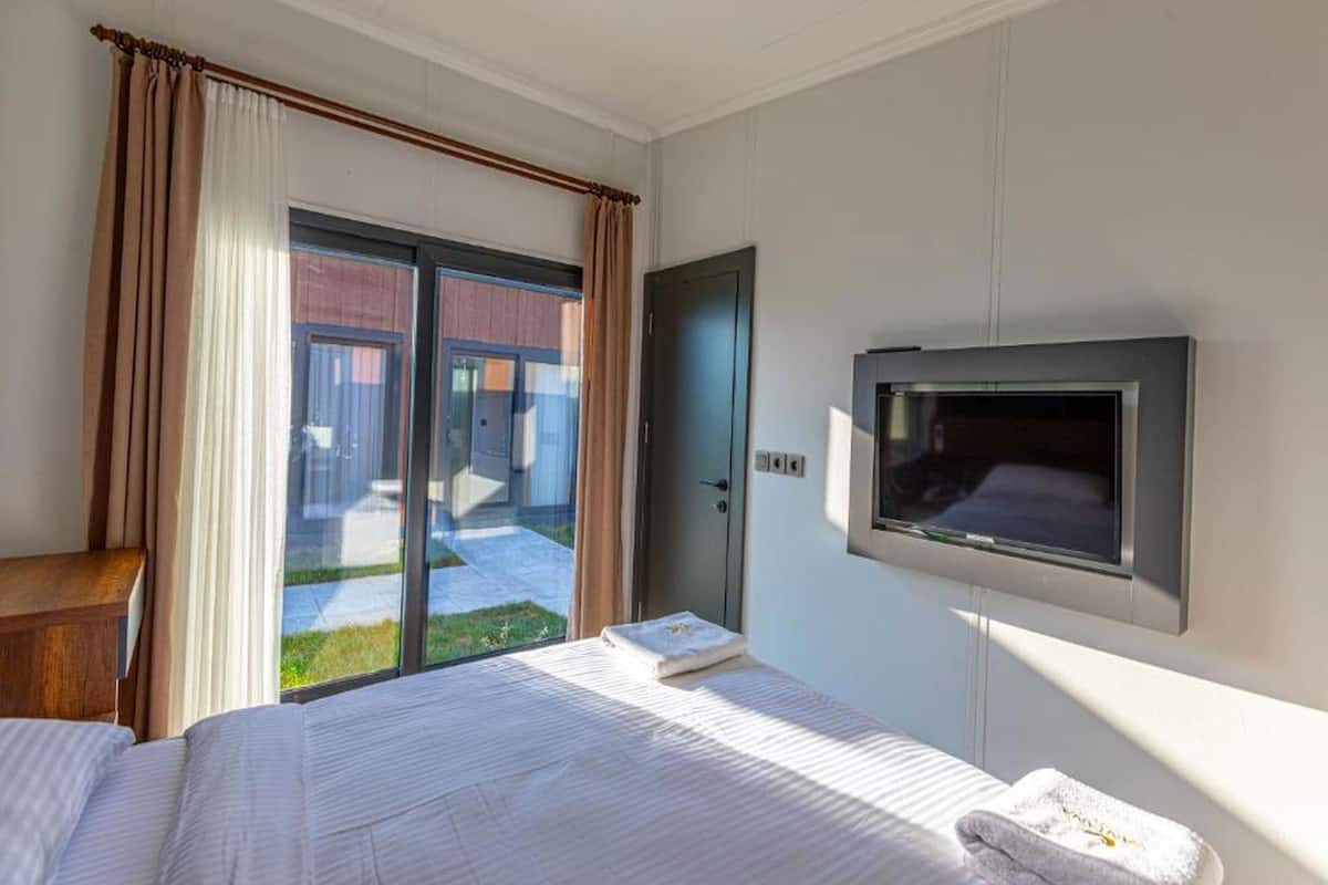 A hotel room with a bed, a TV, a door, and a view of the outside.