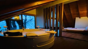 Una habitación con una bañera de hidromasaje circular, un sofá y una ventana con vistas a árboles.