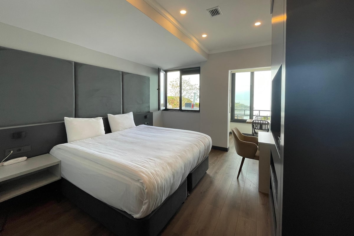 A modern hotel room with a large bed, bedside table, and a view of the outdoors.