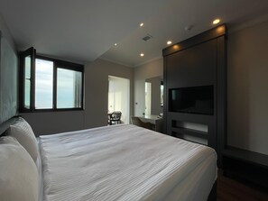 Une chambre d’hôtel dotée d’un grand lit, d’un téléviseur fixé au mur, d’un bureau avec une chaise et d’une fenêtre offrant une vue sur le ciel.