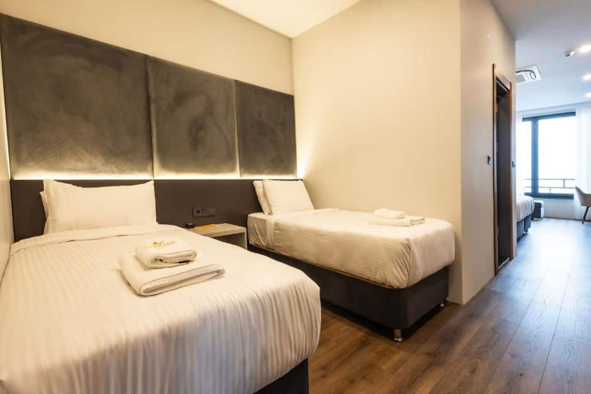 A hotel room with two beds, a large headboard, a nightstand, and a view of the outside.