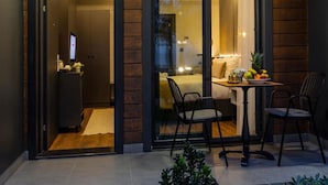 Una habitación de hotel moderna con una cama, un escritorio con una silla, una mesita con fruta y vistas a través de un ventanal.