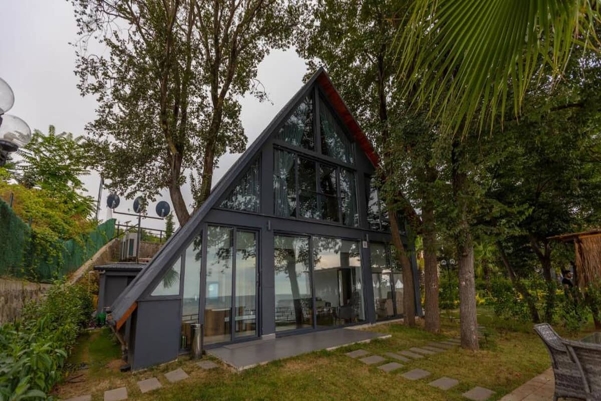 A modern building with large glass windows, a sloped roof, and a small outdoor seating area.