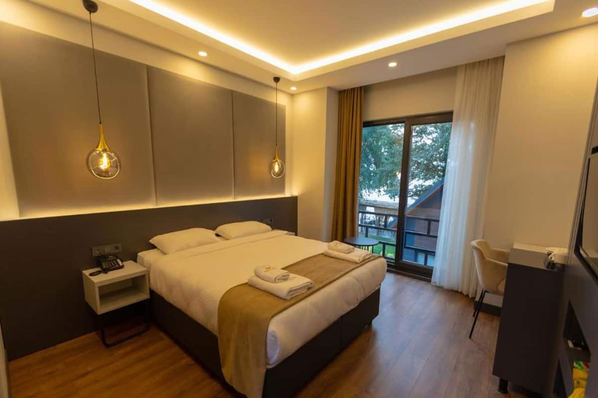 A modern hotel room with a large bed, bedside tables, a desk, and a balcony with a view.