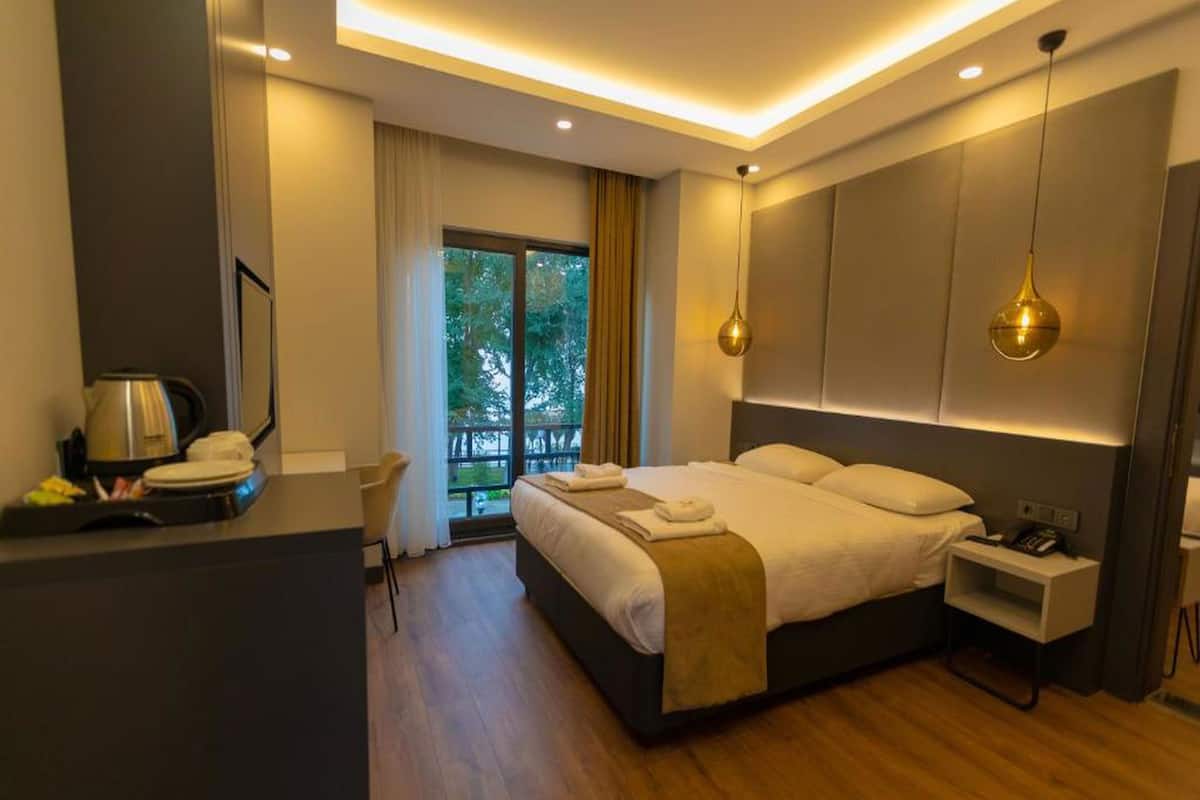 A modern hotel room with a large bed, bedside table, and a view of the outdoors.