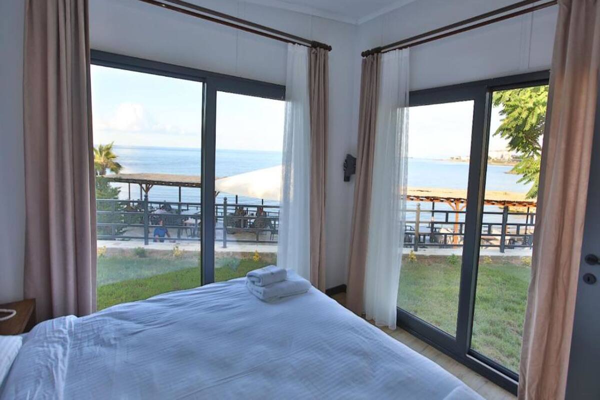 A hotel room with a bed, large windows, and a view of the beach.