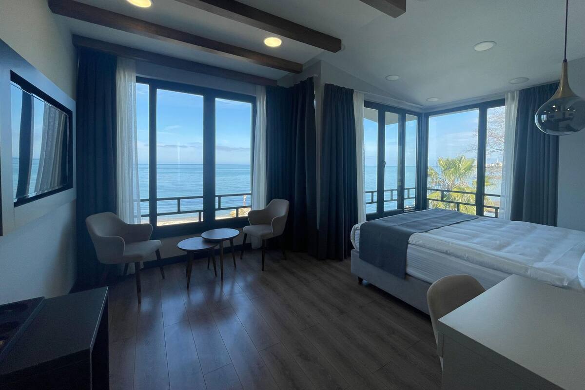A hotel room with a large bed, a desk, two chairs, and a view of the sea.