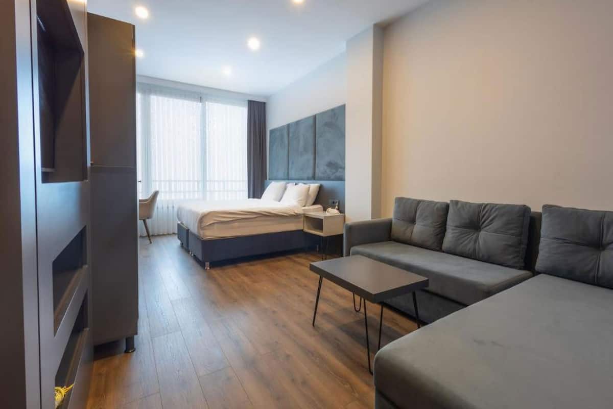 A modern hotel room with a bed, a sofa, a small table, and a TV.