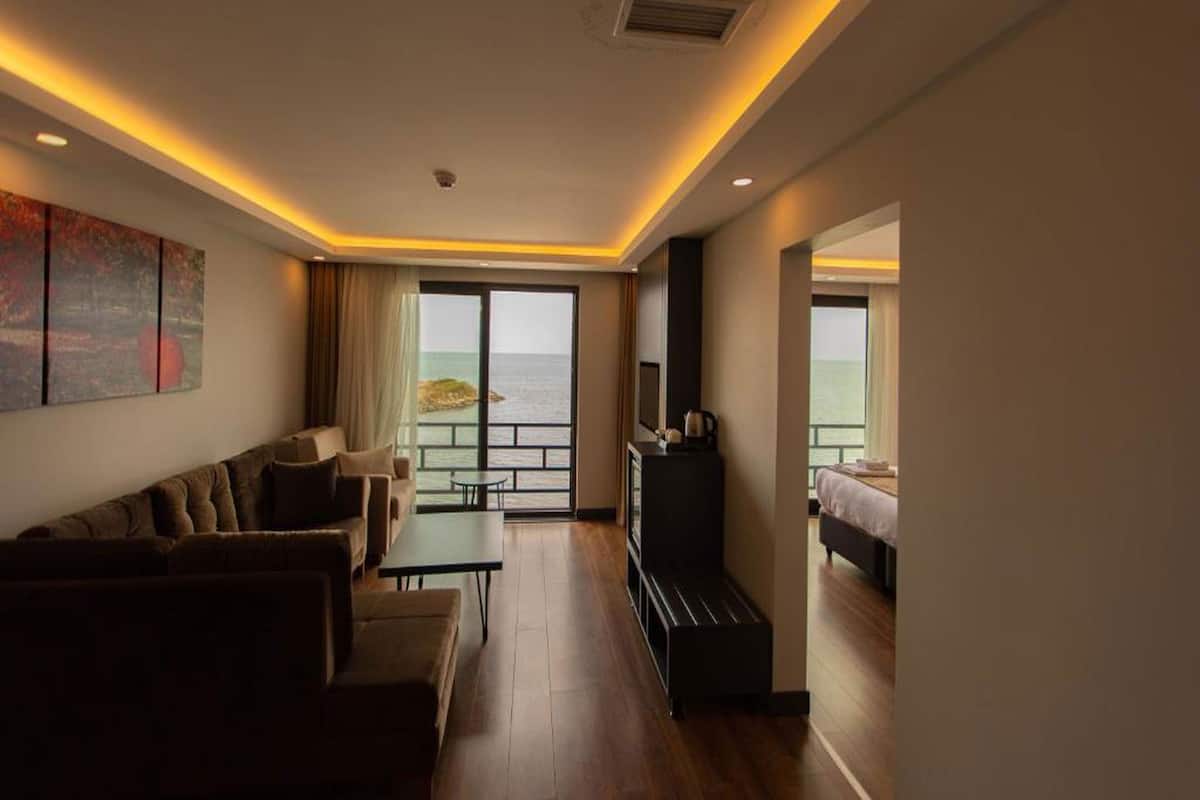 A hotel room with a sofa, a small table, a TV, and a balcony with a view of the sea.