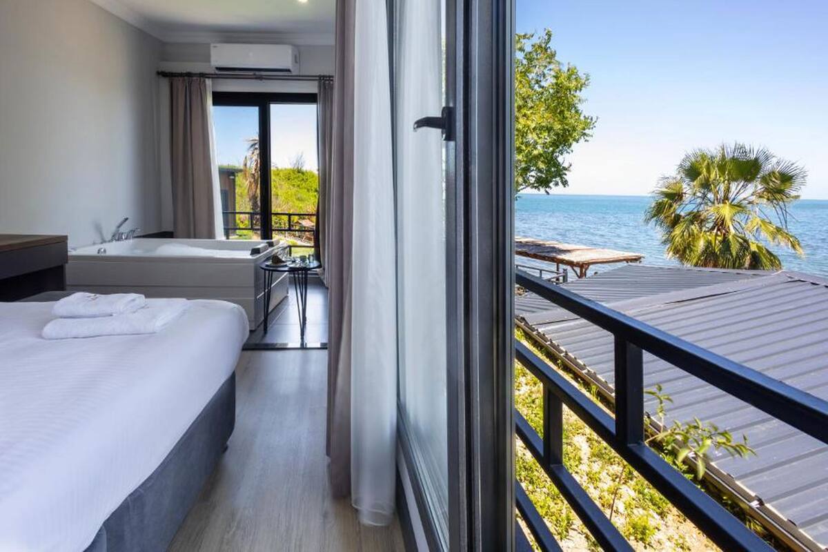 A hotel room with a balcony, a bathtub, and a view of the sea.