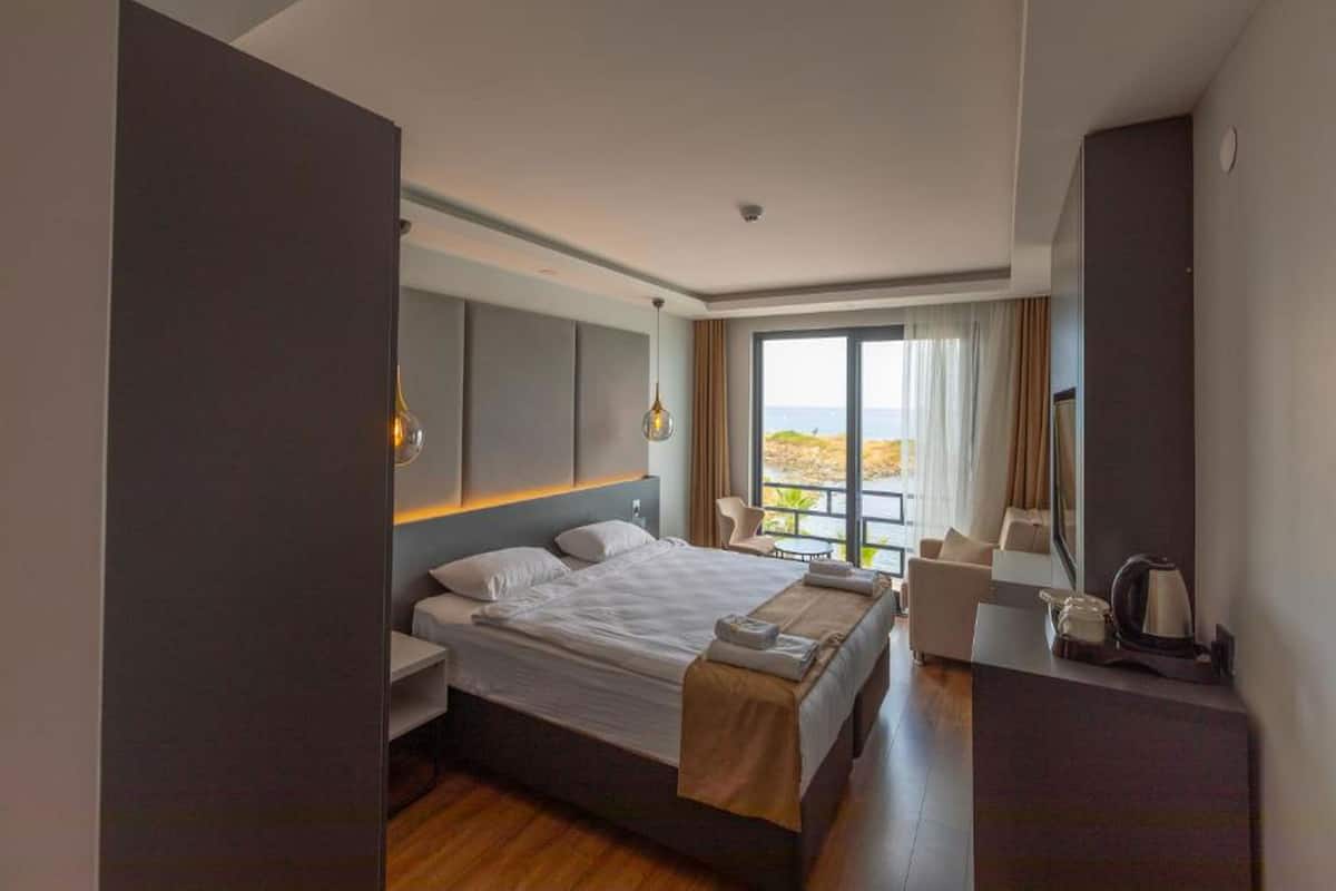 A modern hotel room with a large bed, a desk, and a view of the sea.