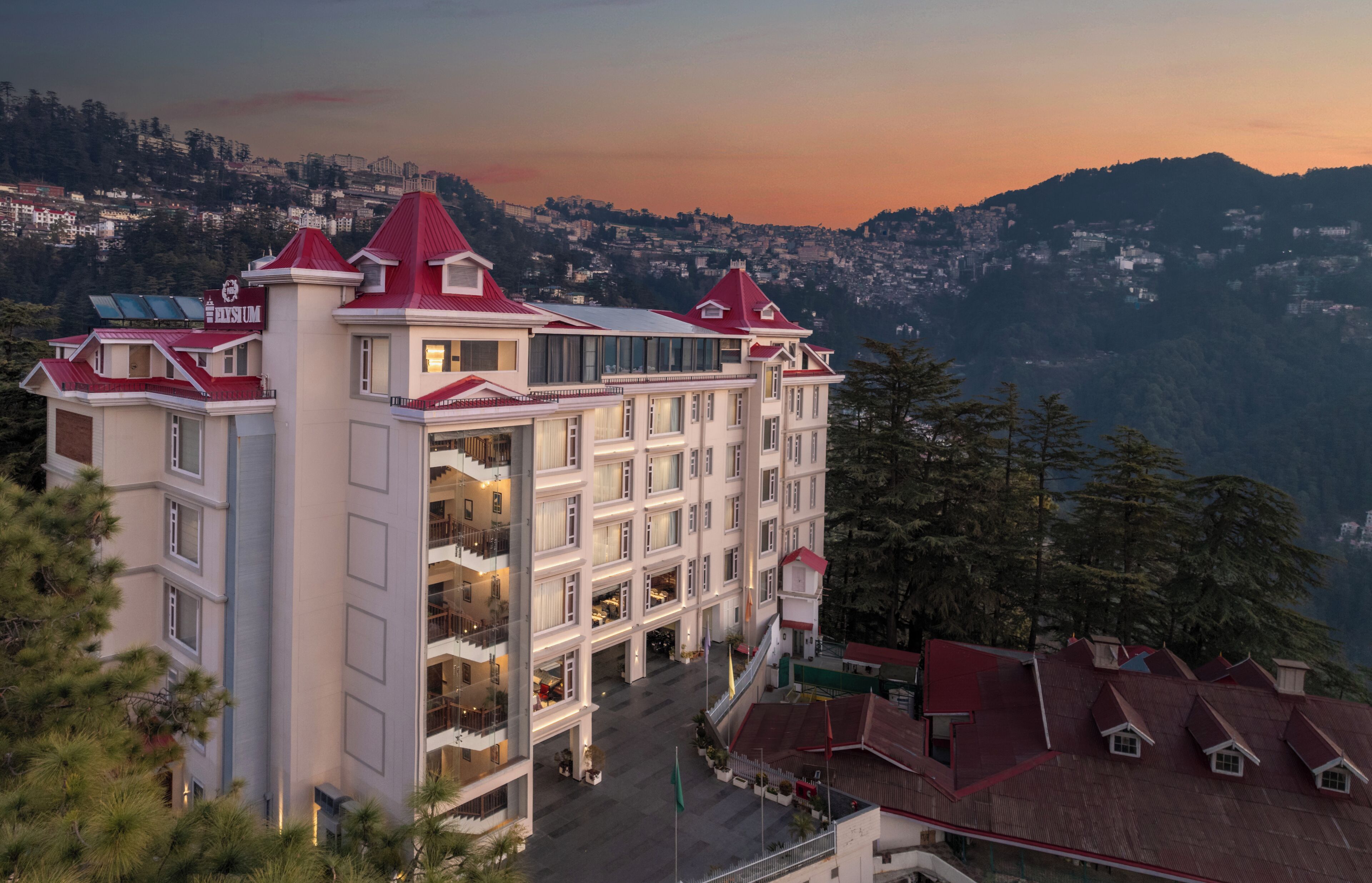 A multi-story hotel with a red roof, multiple balconies, and a view of a mountainous landscape.