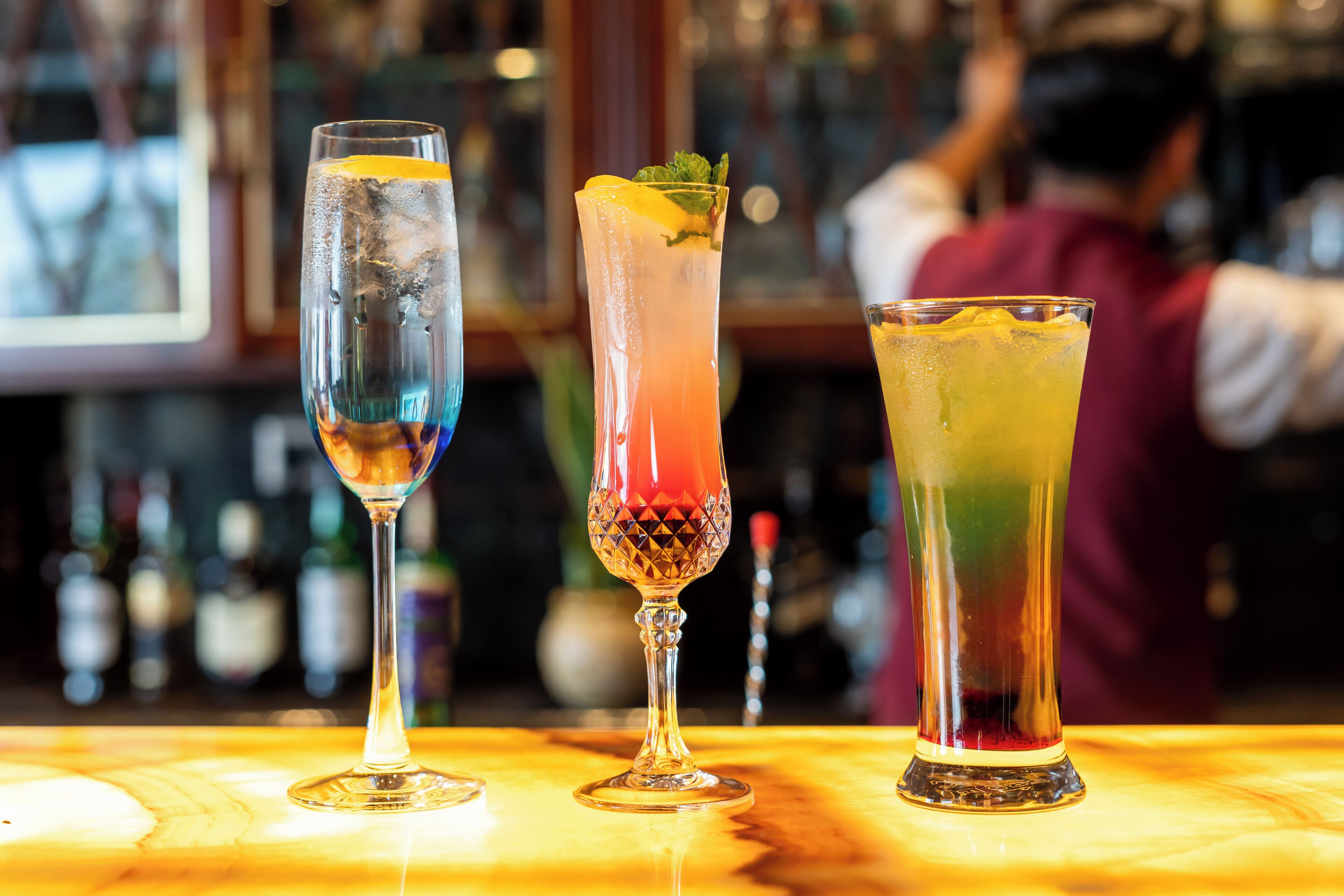 Three glasses of different beverages on a bar counter.