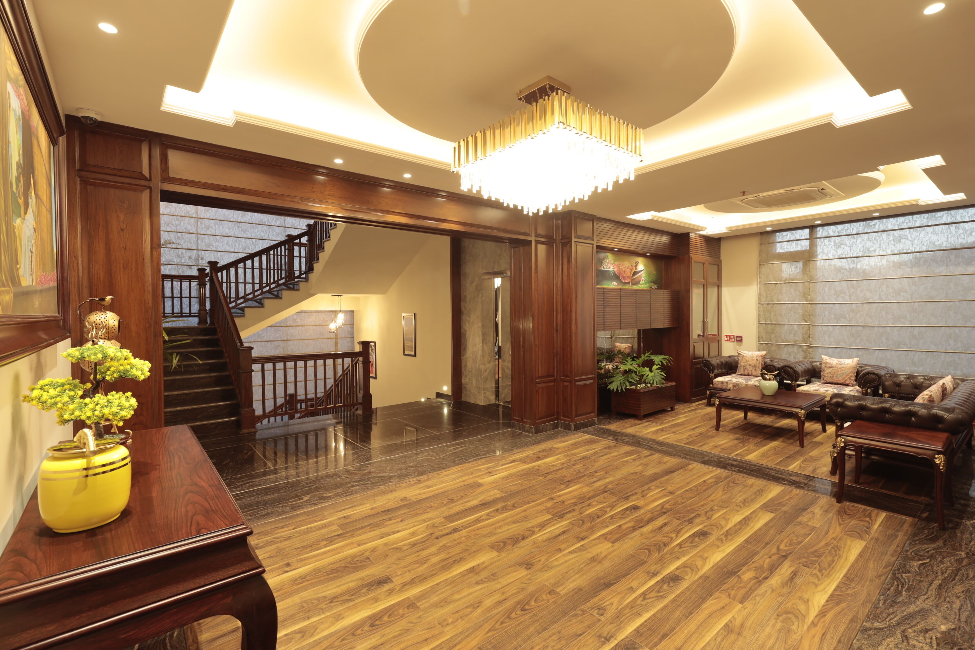 A spacious living area with a wooden floor, a staircase, a chandelier, and a sofa set.
