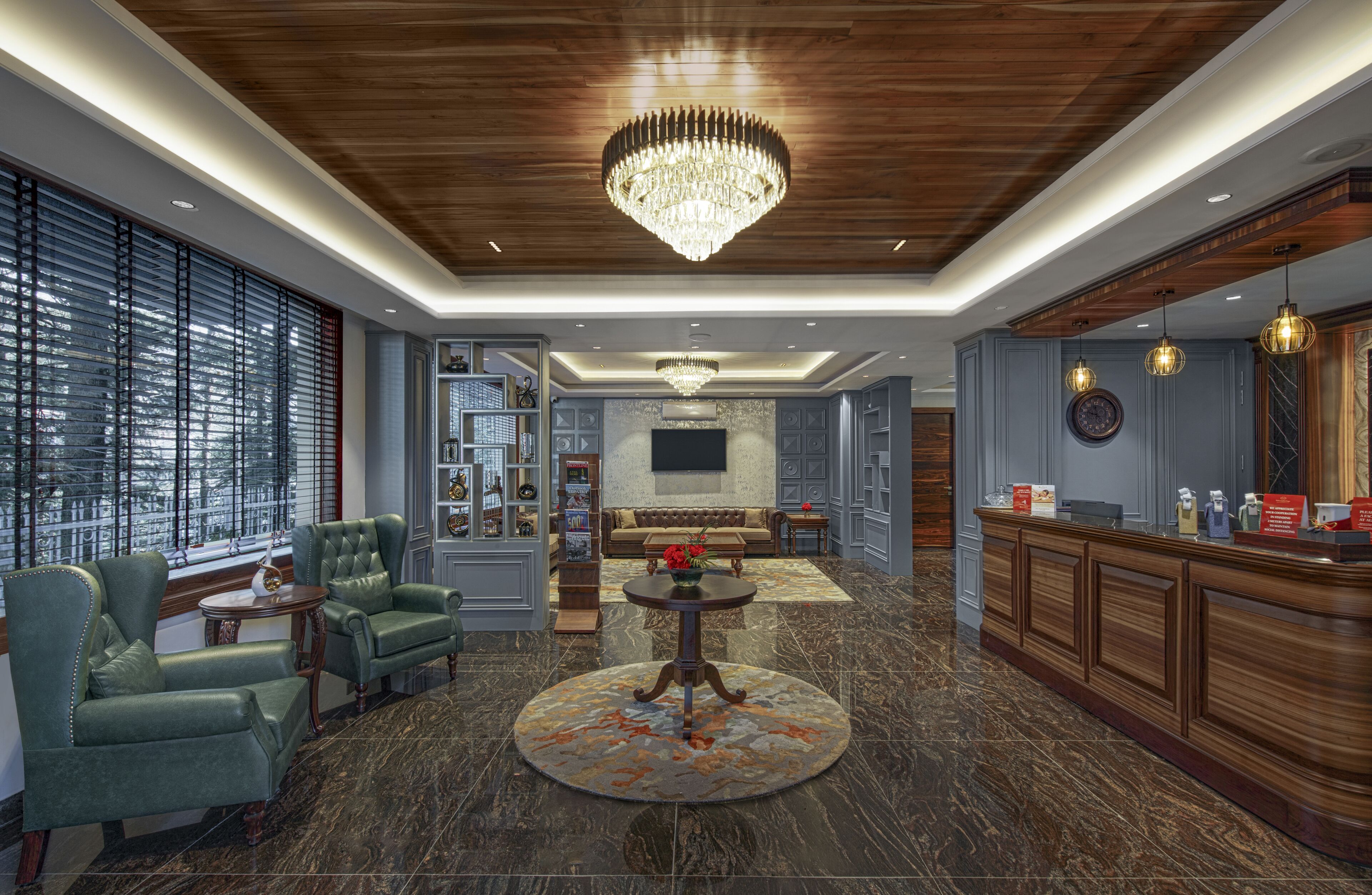 A spacious lobby with a grand chandelier, leather seating, a reception desk, and a large TV screen.