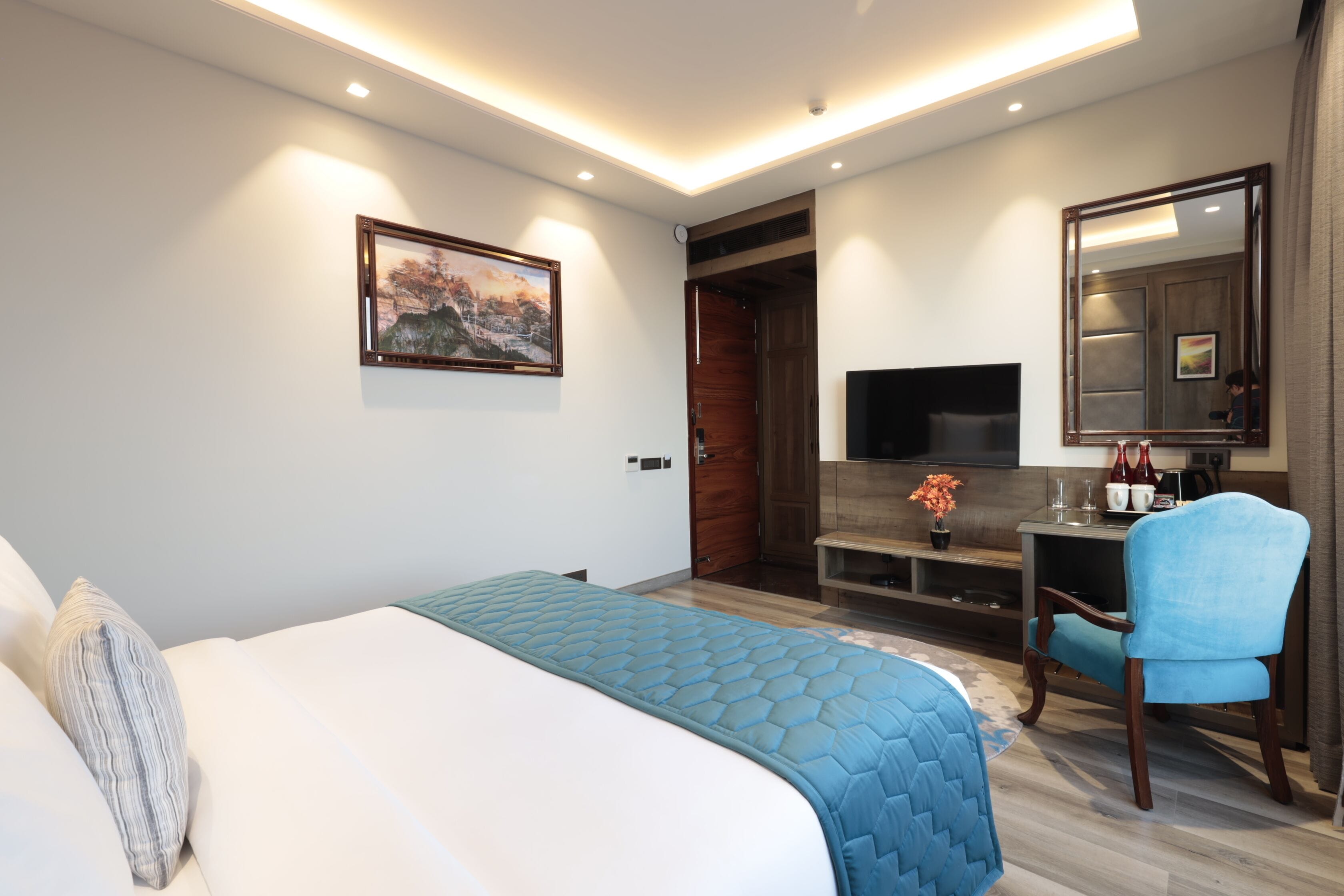Una habitación de hotel moderna con una cama grande, un escritorio con silla, un televisor de pantalla plana y un cuadro en la pared.