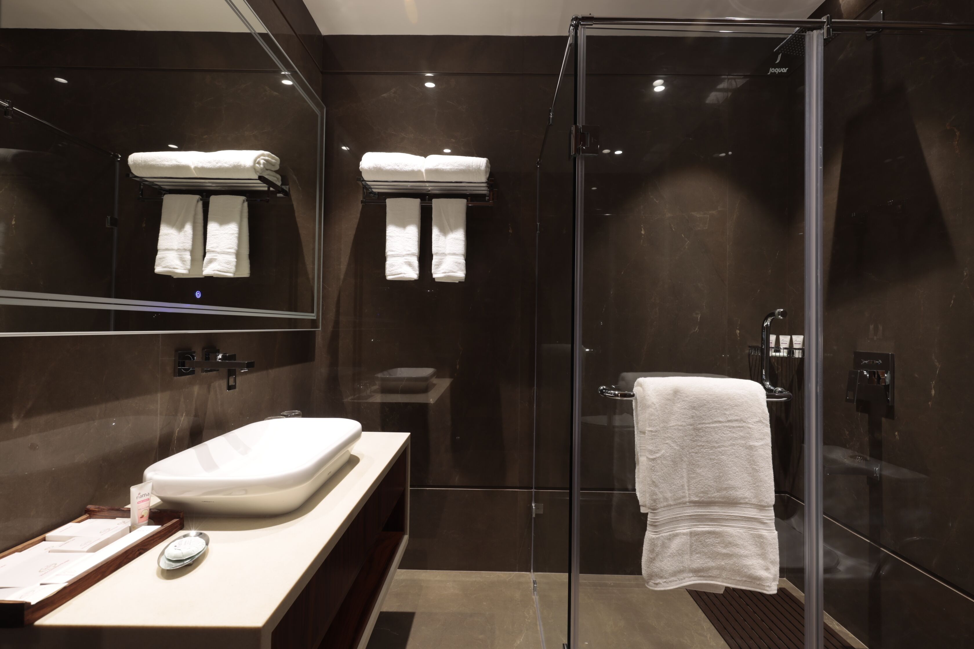 A modern bathroom with a glass-enclosed shower, a large mirror, and a vanity with a sink and towel rack.