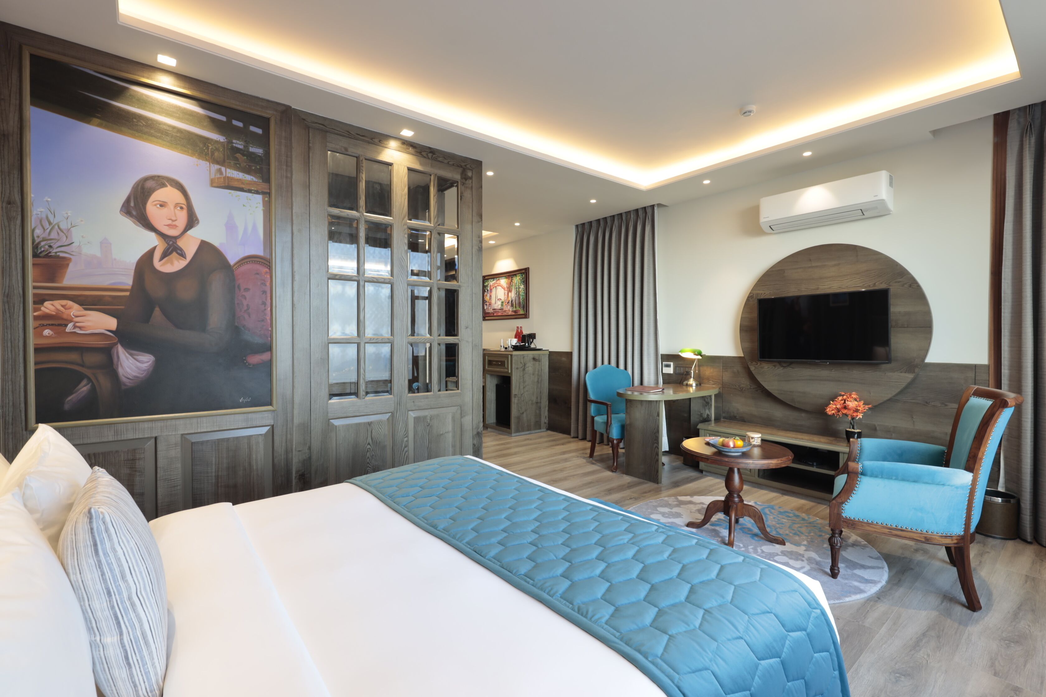 Ein modernes Hotelzimmer mit einem großen Bett, einem Schreibtisch, einem Sessel, einem Fernseher und einem Gemälde an der Wand.