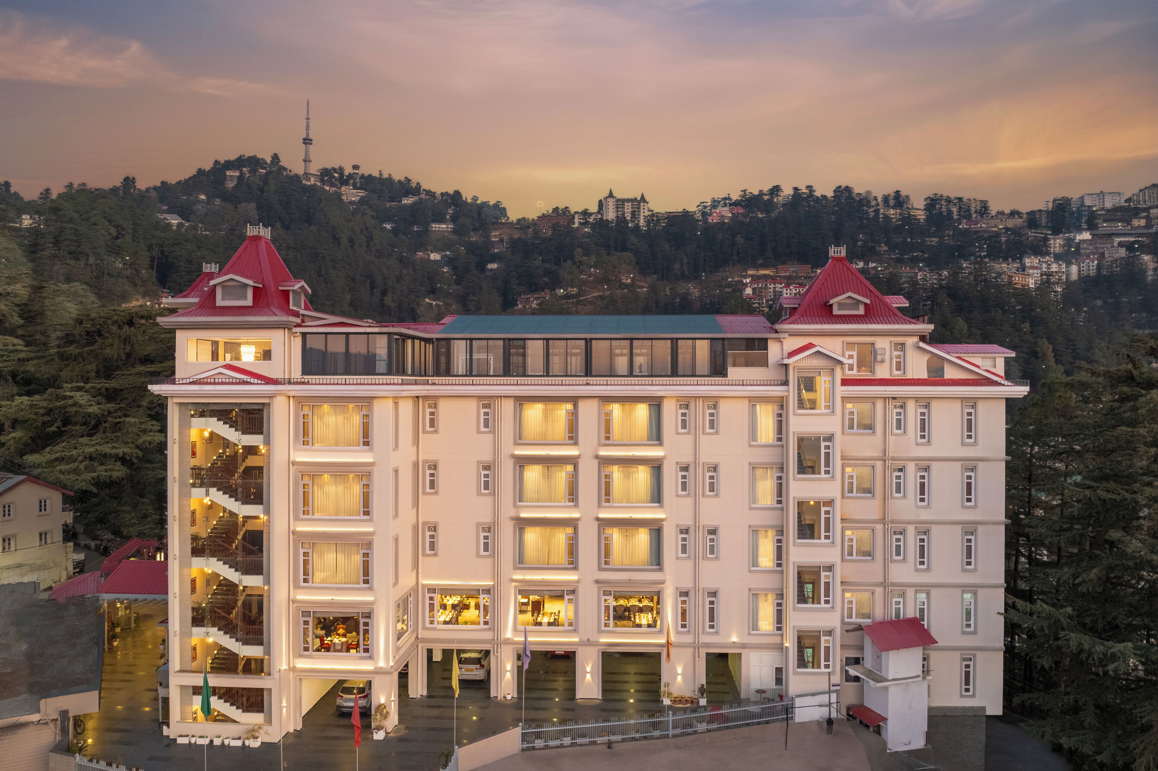 A multi-story hotel with a central atrium, balconies, and a view of a hill with a tower.