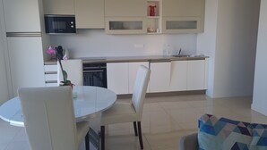 Cozinha moderna com armários brancos, micro-ondas e máquina de lavar louça. Há uma mesa redonda com cadeiras e uma pequena planta em vaso.