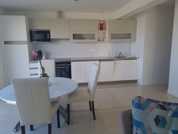 A modern kitchen with white cabinets, a microwave, and a dishwasher. There is a round table with chairs and a small potted plant. - Private accommodation with an exceptional ocean view (Nice)