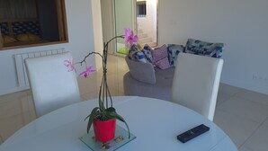 Uma área de refeições com uma mesa redonda, cadeiras, um vaso de planta e um controle remoto.