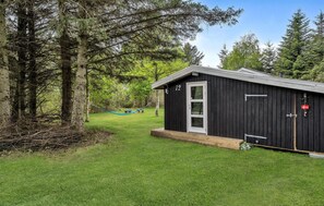 A small black cabin with a white door, surrounded by a grassy yard and trees. - 4 bedroom gorgeous home in ålbæk (Ålbæk)
