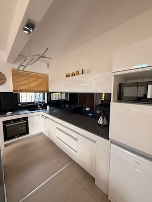 A modern kitchen with white cabinetry, a built-in oven, a Bosch dishwasher, and a window with blinds.