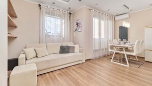 A modern living room with a sofa, dining table, and chairs, wooden flooring, and a ceiling with recessed lighting.