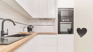 A modern kitchen with white cabinets, a wooden countertop, a black faucet, a coffee maker, a microwave, and an oven.