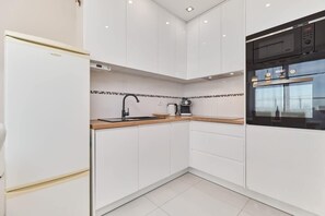 A modern kitchen with white cabinetry, a wooden countertop, a black faucet, and a microwave.
