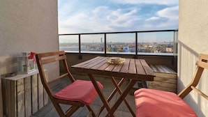 A balcony with a wooden table and two chairs, a lantern, and a city view.