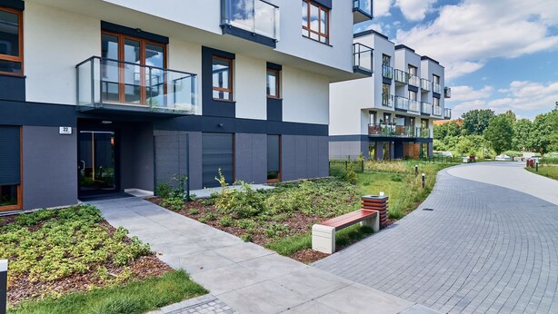 Un moderno edificio residencial de varios pisos con balcones, un sendero pavimentado y un jardín ajardinado.