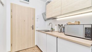 Cocina compacta con puerta de madera, armarios blancos, microondas y fregadero.