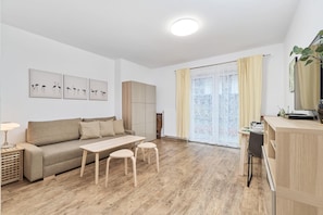 A modern living room with a sofa, coffee table, and stools, a dining area with a table and chairs, and a kitchen area with cabinets and a countertop.