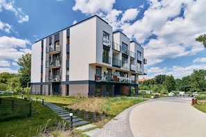 A modern multi-story residential building with balconies, a paved driveway, and a landscaped garden.