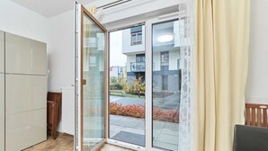 Una habitación con puerta corrediza de vidrio que da a un balcón, una silla de madera y un radiador.